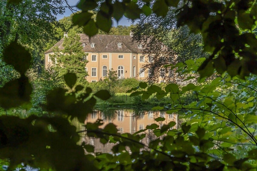 Blick auf das Schloss Rheder, das Gebäude spiegelt sich im Teich des Schlossparks. Fotorechte Stadt Brakel 